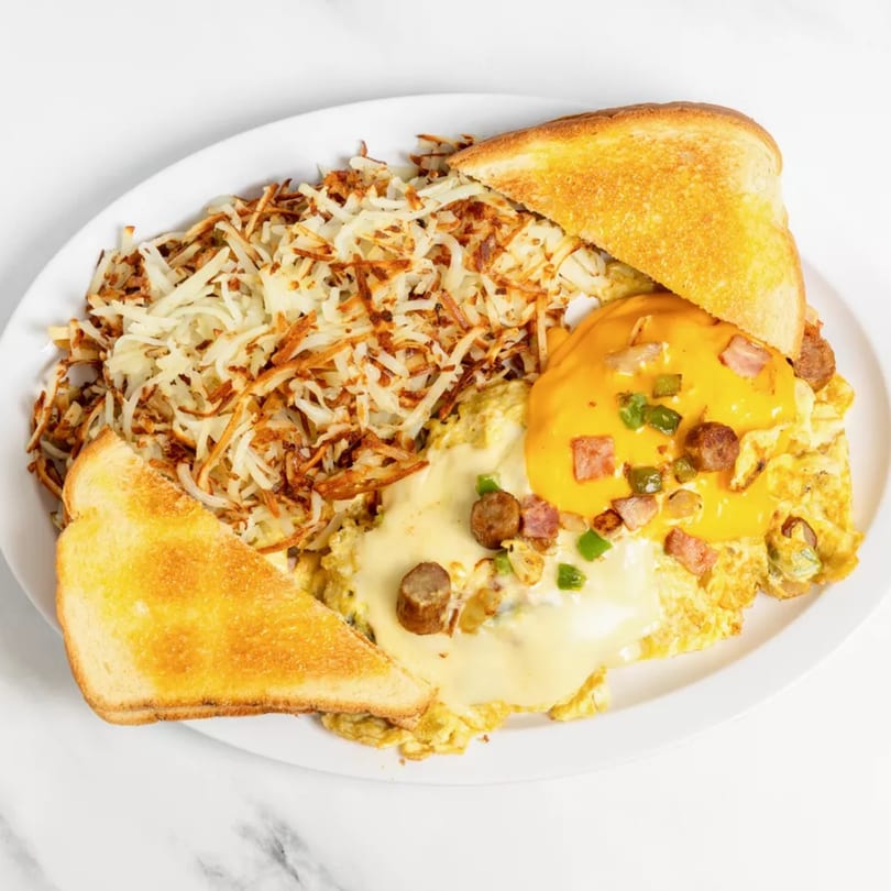 Hearty breakfast platter with hash browns, cheesy omelet topped with sausage and ham, and buttered toast.