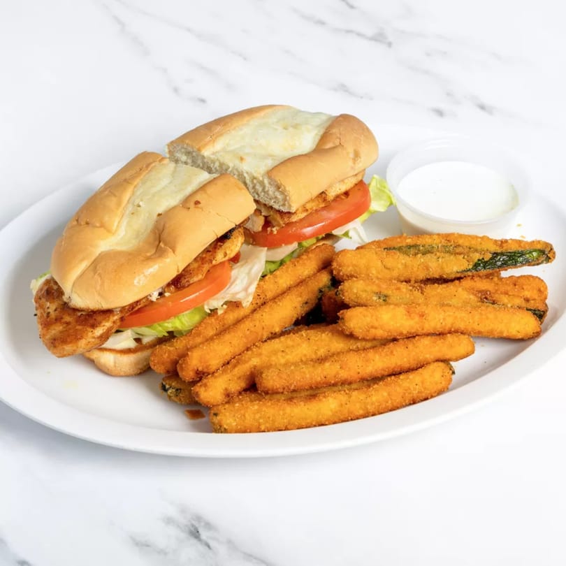 A chicken sandwich with lettuce and tomato, served with a side of fried zucchini sticks and dipping sauce.