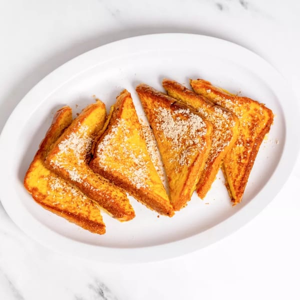 Six triangular pieces of golden French toast, dusted with powdered sugar and cinnamon, on a white plate.