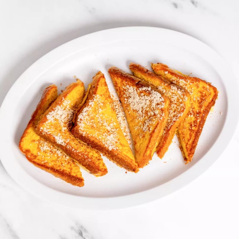 Six triangular pieces of golden French toast, dusted with powdered sugar and cinnamon, on a white plate.